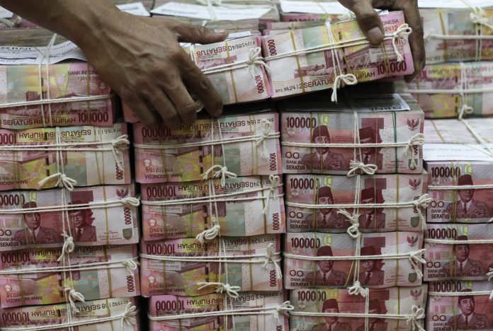 An employee of PT Bank Negara Indonesia Tbk. moves a pack of 100,000 Rupiah notes at the bank's head office in Jakarta